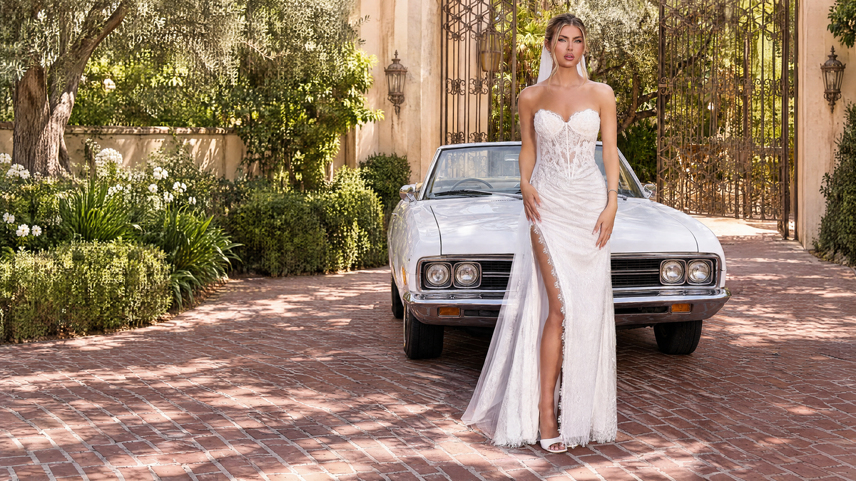 Bride in the Walters off-white lace gown beside a white vintage convertible.